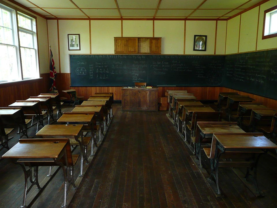 Sala de aula antiga, como carteiras vazias, lousa escrita, sem professor