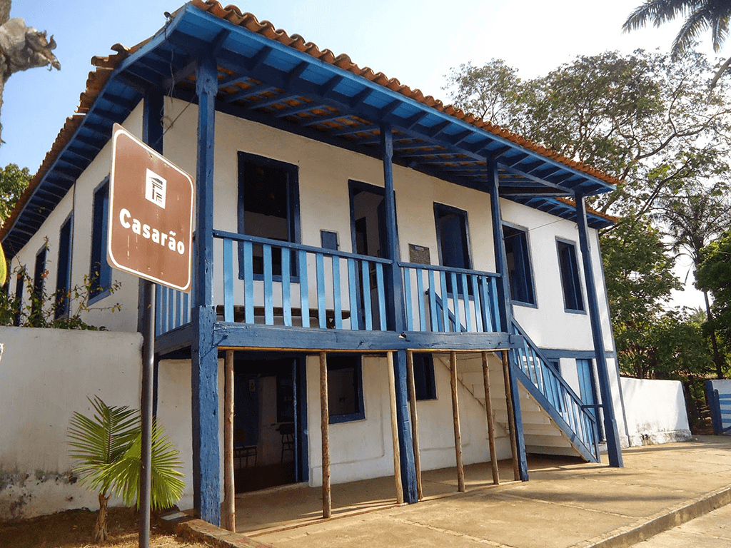 Casarão antigo com paredes brancas e uma sacada de madeira azul. 